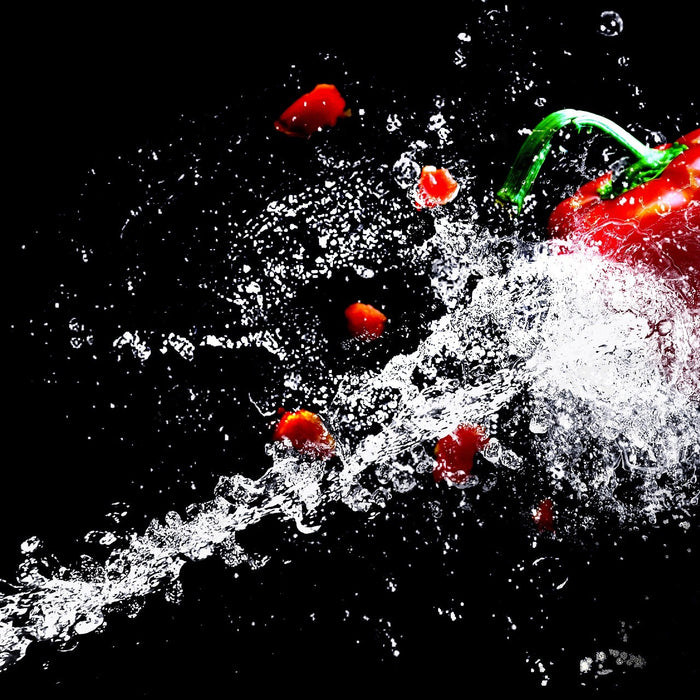 Red bell pepper being splashed by water on a black background