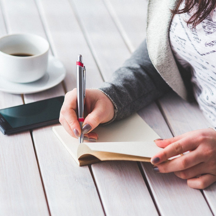 Woman taking notes on a notepad sitting next to her phone and a coffee