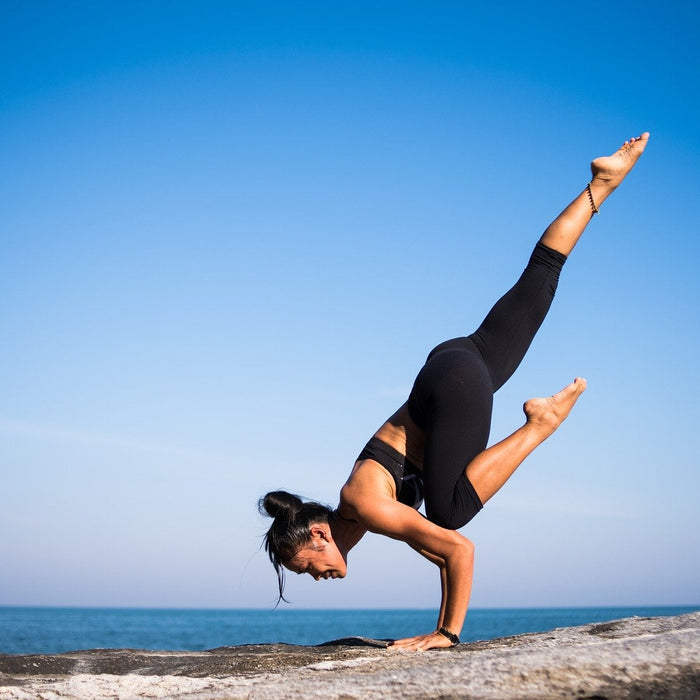 Woman doing yogo and standing in one hand next to a beach
